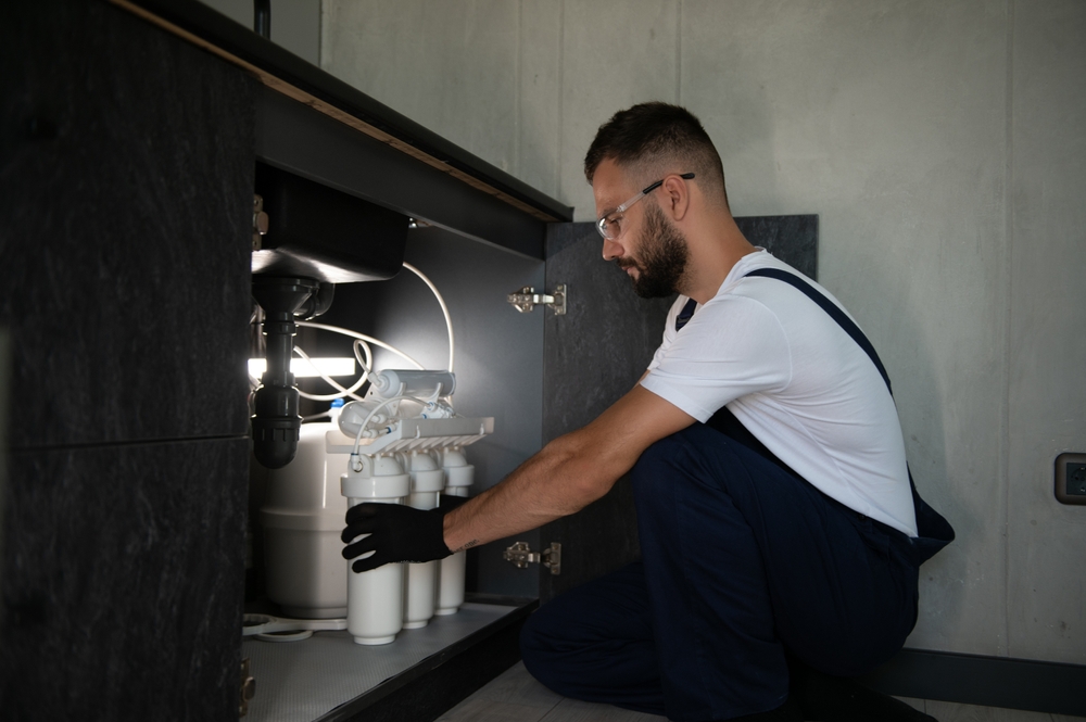 Plumber working install new cartridge for cold water filter in white kitchen.