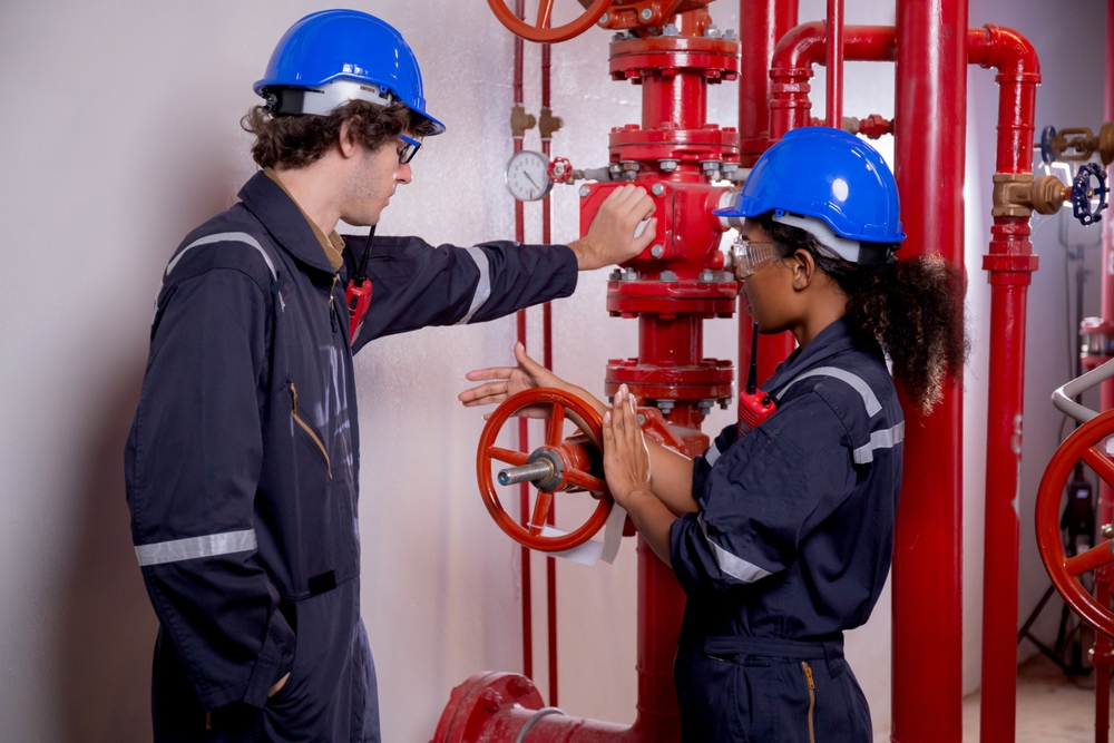 Young woman and man engineer check and examining pipeline and discussion in the factory, mechanic or technician inspector plumber valve and talking together, industrial and maintenance concept.
